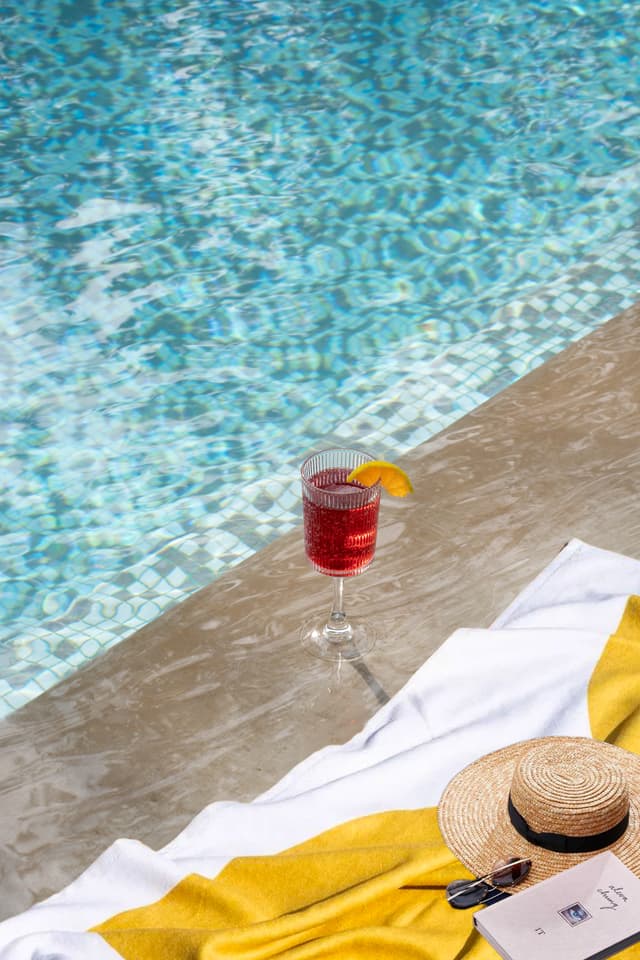A refreshing red cocktail and a straw hat placed beside the sparkling pool at Saj in the Forest, Pench.