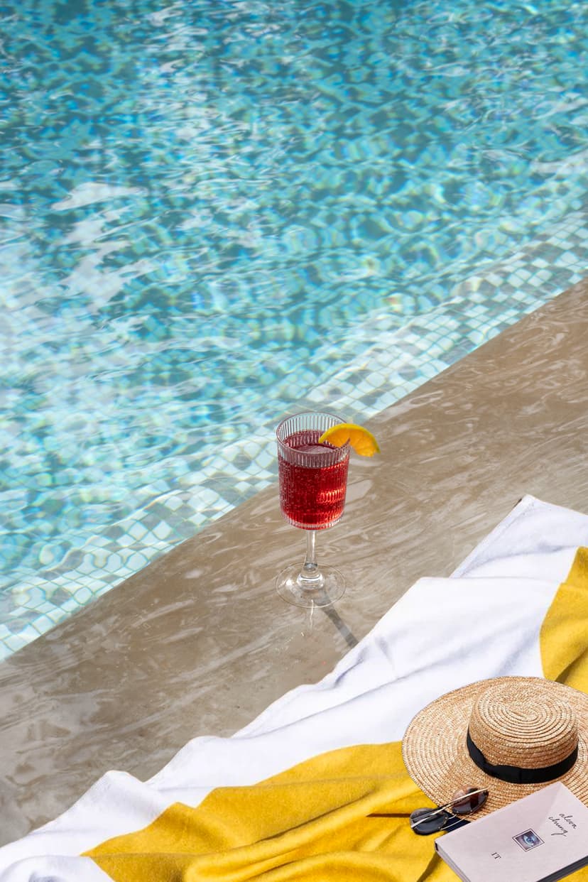 A refreshing red cocktail and a straw hat placed beside the sparkling pool at Saj in the Forest, Pench.