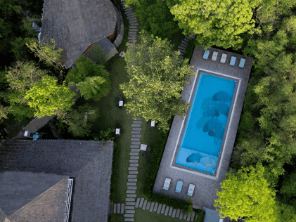 Aerial view of Saj in the Forest resort pool area and cottages surrounded by dense green trees in Pench National Park.