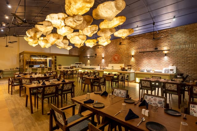 Warmly lit interior of Maati Baani restaurant at Saj By The Lake featuring unique cloud-shaped pendant lights and exposed brick walls.
