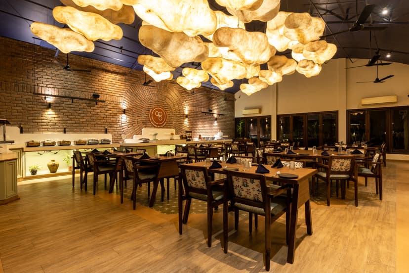 Spacious dining hall of Maati Baani restaurant at Saj By The Lake with cloud pendant lights, wooden furniture and a buffet counter.