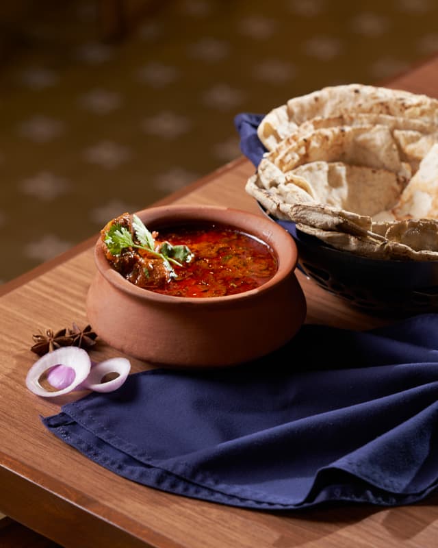 Traditional Indian curry served in a clay pot with rotis on a wooden board at Maati Baani restaurant, Saj By The Lake.