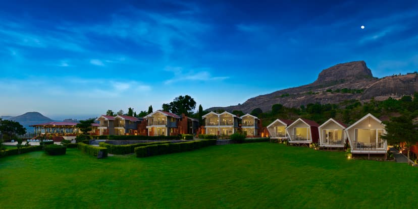 Panoramic twilight view of Saj By The Lake resort cottages and manicured lawns with the Sahyadri mountains in the background, Malshej Ghat.