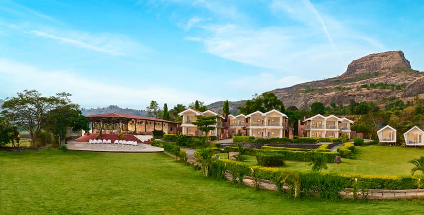 Daytime panoramic view of Saj By The Lake resort grounds featuring an open-air amphitheatre, guest villas and the Sahyadri mountain backdrop.