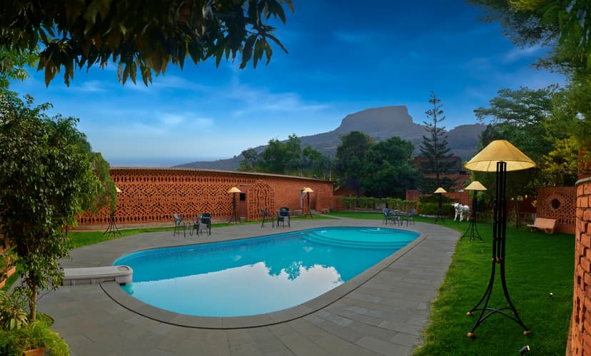 Outdoor swimming pool at Saj By The Lake surrounded by brick lattice walls, garden lamps and a scenic Sahyadri mountain view at dusk.