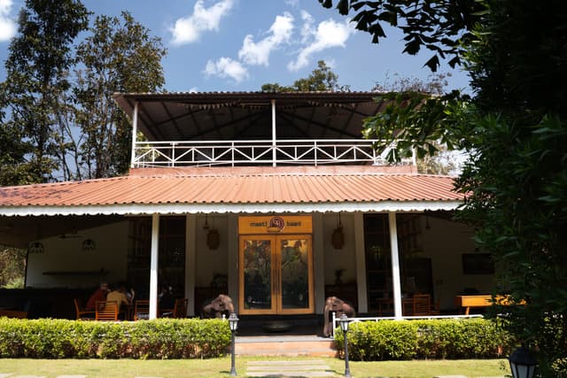 Daytime exterior of Maati Baani restaurant at Saj in the Forest, Pench, framed by garden greenery under a blue sky.