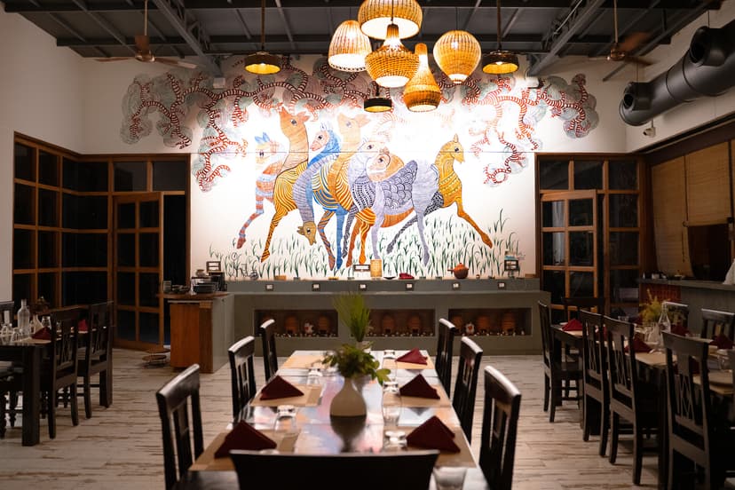 Elegantly set dining area inside Maati Baani restaurant at Saj in the Forest with a dramatic Pichwai-inspired mural of horses.