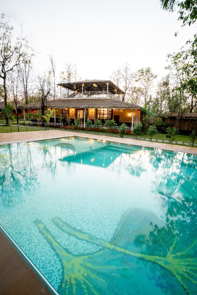 Sparkling swimming pool at Saj in the Forest, Pench, with the resort building and lush greenery reflected in the calm water.