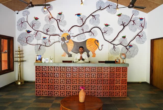 Reception lobby of Saj in the Forest featuring a hand-painted Gond art mural of a tiger, colourful birds and forest trees.